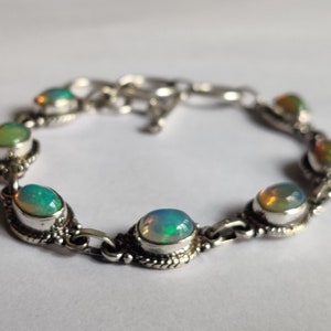 May include: A silver bracelet with seven oval-shaped opal gemstones. The bracelet has a clasp closure.