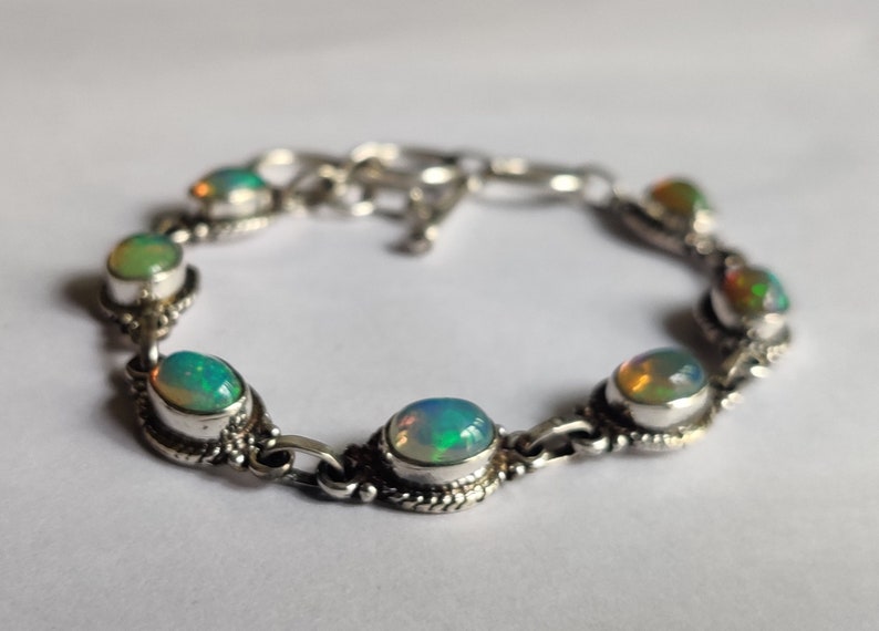 May include: A silver bracelet with seven oval-shaped opal gemstones. The bracelet has a clasp closure.