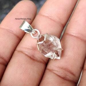 Op de afbeelding: Een zilveren hanger met een heldere, gefacetteerde Herkimer-diamant. De diamant is gezet in een zilveren bezel en heeft een unieke, geometrische vorm.
