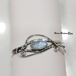 May include: A silver bracelet with a delicate, intricate design featuring a large oval moonstone and two smaller moonstones. The bracelet is made of sterling silver and has a polished finish.