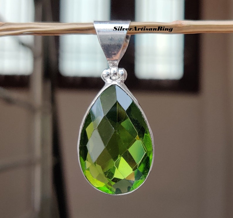 May include: A silver pendant with a teardrop-shaped green gemstone. The gemstone is faceted and has a high shine.
