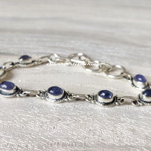 May include: A silver bracelet with a chain link design and oval-shaped purple gemstones. The bracelet has a clasp closure.