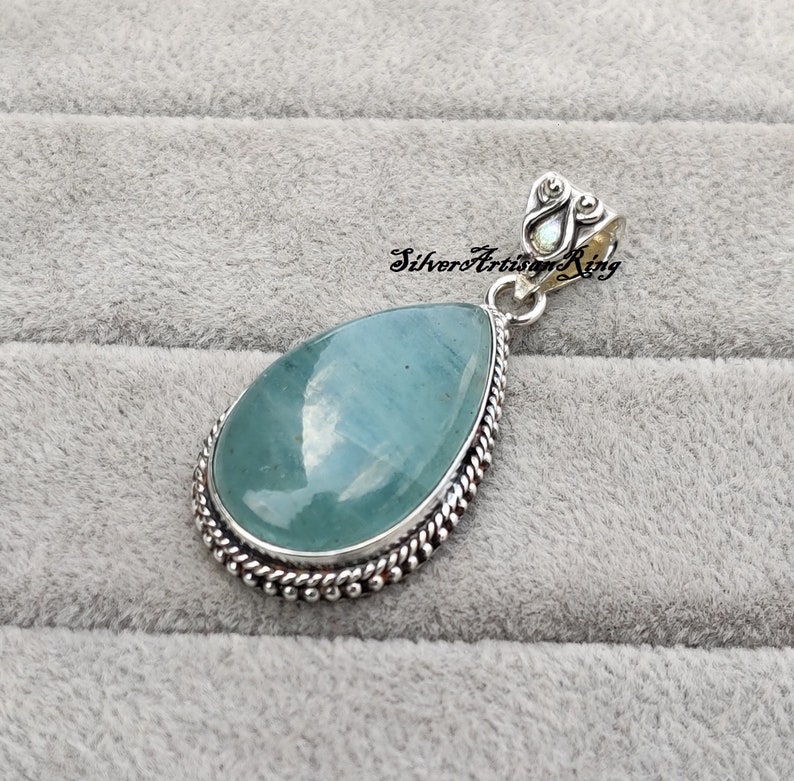 May include: A teardrop-shaped pendant with a light blue aquamarine gemstone set in a silver bezel. The pendant has a silver bail with a decorative design.