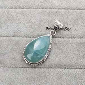 May include: A teardrop-shaped pendant with a light blue aquamarine gemstone set in a silver filigree frame. The pendant is on a gray background.