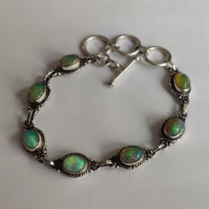 May include: A silver bracelet with a toggle clasp features six oval-shaped green opals.