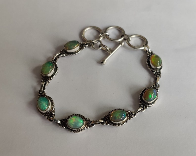 May include: A silver bracelet with a toggle clasp features six oval-shaped green opals.