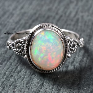 May include: A silver ring featuring a white opal gemstone set in an intricate bezel. The ring band is adorned with a twisted rope design.