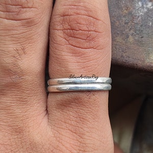 Könnte beinhalten: Nahaufnahme eines silbernen Rings, der an einem Finger getragen wird. Der Ring ist ein schlichtes Band mit leicht gehämmerter Textur. Der Text "Silver Artisan Ring" ist auf dem Ring sichtbar.