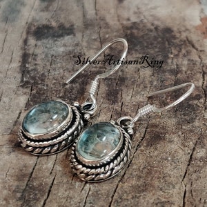 May include: Silver earrings with a blue gemstone set in a silver bezel with a rope-like design. The earrings have a hook closure.