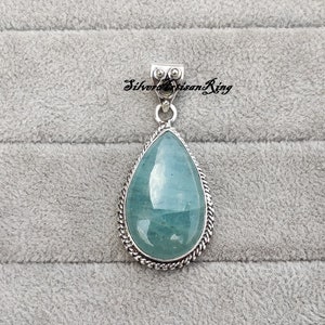 May include: A teardrop-shaped pendant with a light blue aquamarine gemstone set in a silver bezel. The pendant has a silver bail with a decorative design.