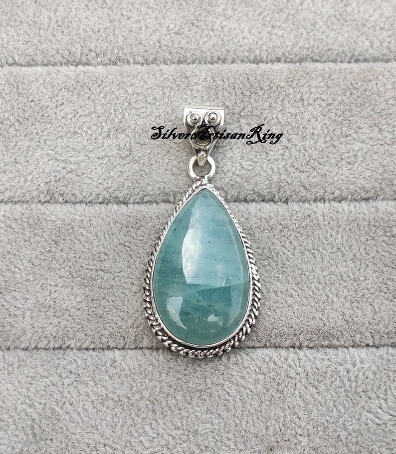 May include: A teardrop-shaped pendant with a light blue aquamarine gemstone set in a silver bezel. The pendant has a silver bail with a decorative design.