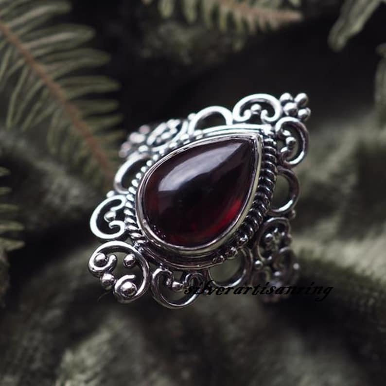 May include: A silver ring with a teardrop-shaped red gemstone set in a filigree design.