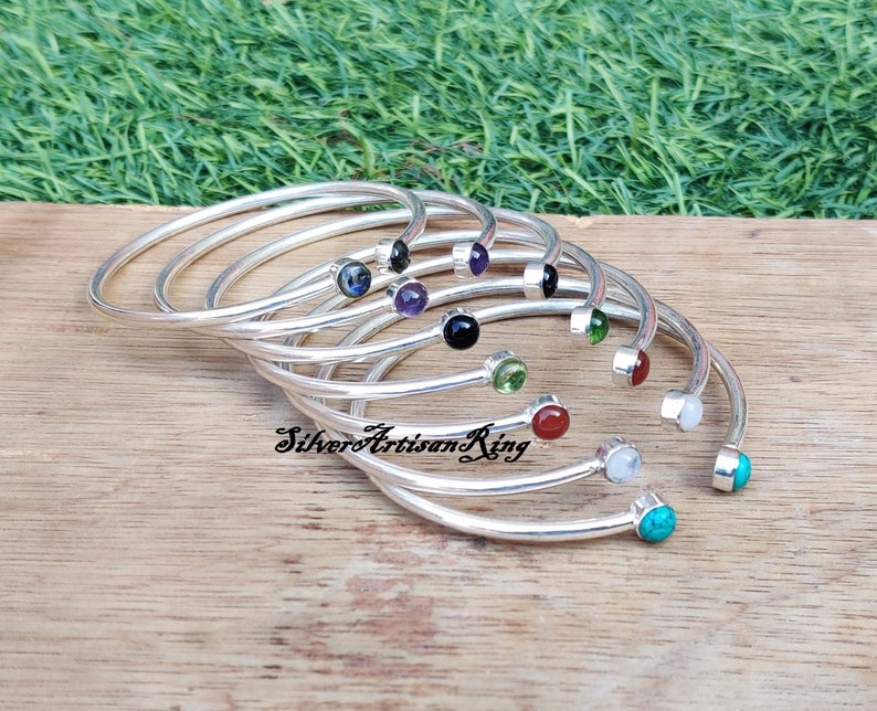 Pode incluir: Um conjunto de pulseiras de prata com pedras preciosas de diferentes cores. As pulseiras est&atilde;o empilhadas umas sobre as outras e as pedras preciosas s&atilde;o vis&iacute;veis. As pedras preciosas s&atilde;o turquesa, branca, vermelha, verde, preta, roxa e azul.