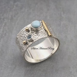 Puede incluir: Un anillo de plata con un diseño texturizado y tres piedras preciosas. El anillo tiene una banda dorada y una piedra preciosa azul. El anillo está inscrito con el texto "Silver Artisan Ring".
