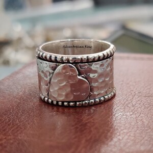 Pu&ograve; includere: Un anello d'argento con finitura martellata e un design a forma di cuore. L'anello &egrave; inciso con le parole "Silverartisan Ring".