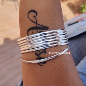 May include: A collection of polished silver bangles. The bracelets have a smooth, reflective surface and a minimalist design. The bangles are stacked, creating a layered effect. The jewellery is a timeless accessory, suitable for various occasions.