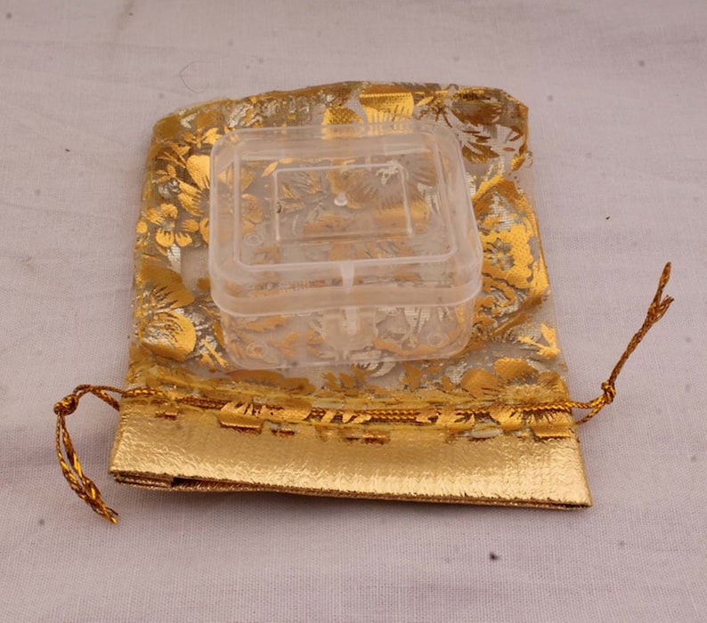May include: A clear plastic square box with a lid, inside a gold and white floral patterned drawstring bag.
