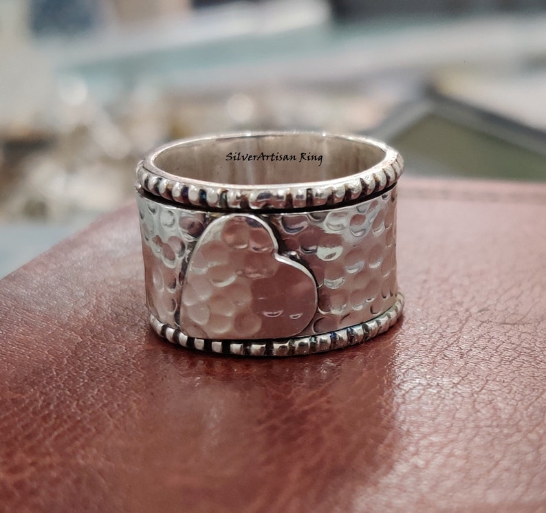 Pu&ograve; includere: Un anello d'argento con finitura martellata e un design a forma di cuore. L'anello &egrave; inciso con le parole "Silverartisan Ring".