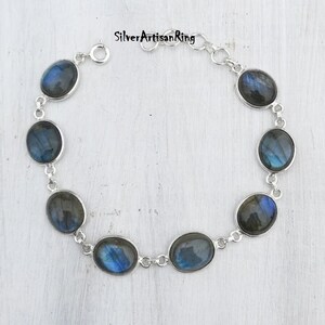 May include: A silver bracelet with a chain link design and oval-shaped labradorite gemstones. The stones have a blue and green iridescent sheen.