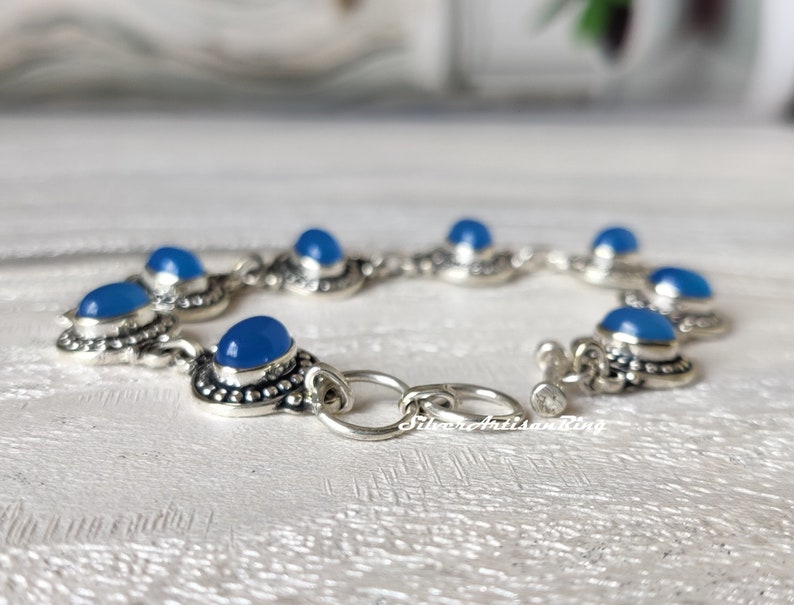 May include: A silver bracelet with blue gemstone accents. The bracelet has a toggle clasp and is made of sterling silver.