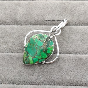 May include: A silver pendant with a green and brown gemstone in a teardrop shape. The pendant is set in a silver frame with a twisted bail.
