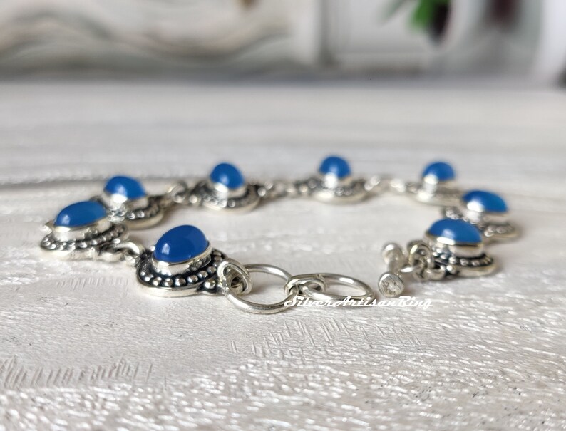 May include: A silver bracelet with blue gemstone accents. The bracelet has a toggle clasp and is made of sterling silver.
