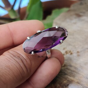 May include: A silver ring with a large, faceted, oval-shaped amethyst gemstone. The ring is set with small silver accents around the gemstone.