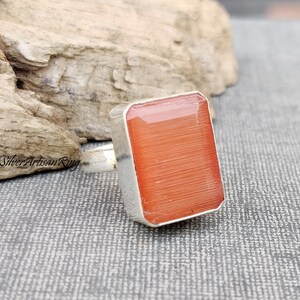 May include: A silver ring featuring a square, orange gemstone. The gemstone has a striated texture.
