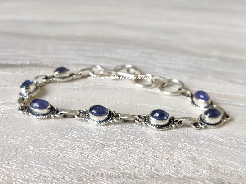 May include: A silver bracelet with a chain link design and oval-shaped purple gemstones. The bracelet has a clasp closure.