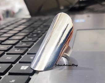 Pode incluir: Um anel de prata com um design liso, arredondado e ligeiramente curvo. O anel está em um teclado de laptop.