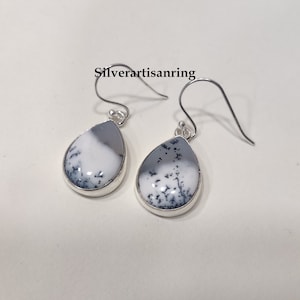 Pu&ograve; includere: Un paio di orecchini pendenti in argento con pietre di agata dendritica a forma di goccia. Le pietre sono bianche con motivi dendritici neri.
