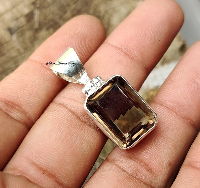 Pode incluir: Um pingente de prata com uma gema marrom. A gema &eacute; cortada em forma de esmeralda e tem um acabamento facetado. O pingente est&aacute; em uma corrente de prata.