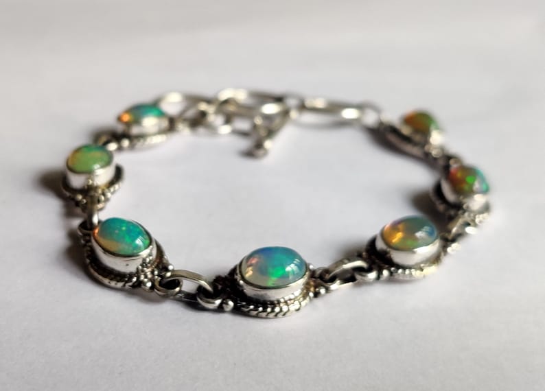 May include: A silver bracelet with seven oval-shaped opal gemstones. The bracelet has a delicate chain design and a lobster clasp.