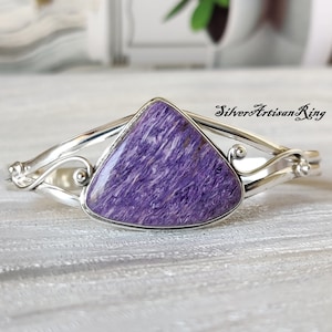 Pode incluir: Uma pulseira de prata com uma gema triangular roxa. A pulseira tem um design delicado e em espiral.