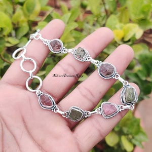 Könnte beinhalten: Silberarmband mit einem Kettenglieddesign und sieben facettierten Edelsteinen. Die Edelsteine sind eine Mischung aus Rosa, Grün und Schwarz.