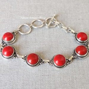 May include: A silver bracelet with a toggle clasp and five red gemstone cabochons. The bracelet has a delicate chain design.