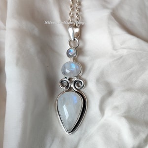 May include: A silver pendant with three moonstone gems. The pendant features a teardrop-shaped moonstone, a round moonstone, and a smaller round moonstone. The pendant is attached to a silver chain.