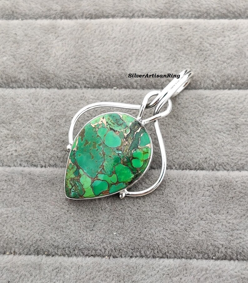 May include: A silver pendant with a green and brown gemstone in a teardrop shape. The pendant is set in a silver frame with a twisted design.