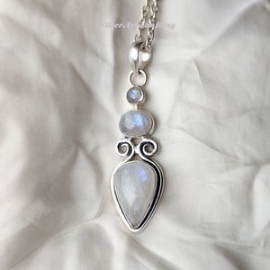 May include: A silver pendant necklace with a teardrop-shaped moonstone and two smaller round moonstones. The pendant is set in a silver filigree design.