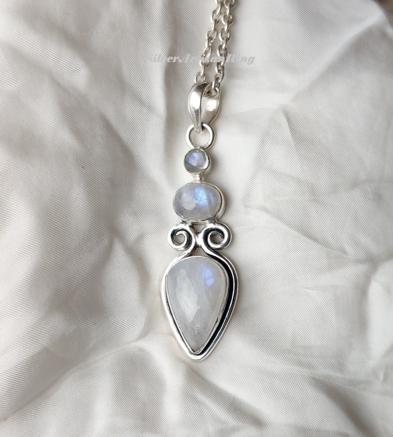 May include: A silver pendant necklace with a teardrop-shaped moonstone and two smaller round moonstones. The pendant is set in a silver filigree design.