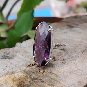 May include: A silver ring with a large, faceted, oval-shaped amethyst gemstone. The ring is set in a simple, elegant design.