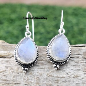 May include: A pair of silver dangle earrings with teardrop-shaped moonstone gemstones. The earrings have a delicate, twisted wire design and are accented with small silver beads.