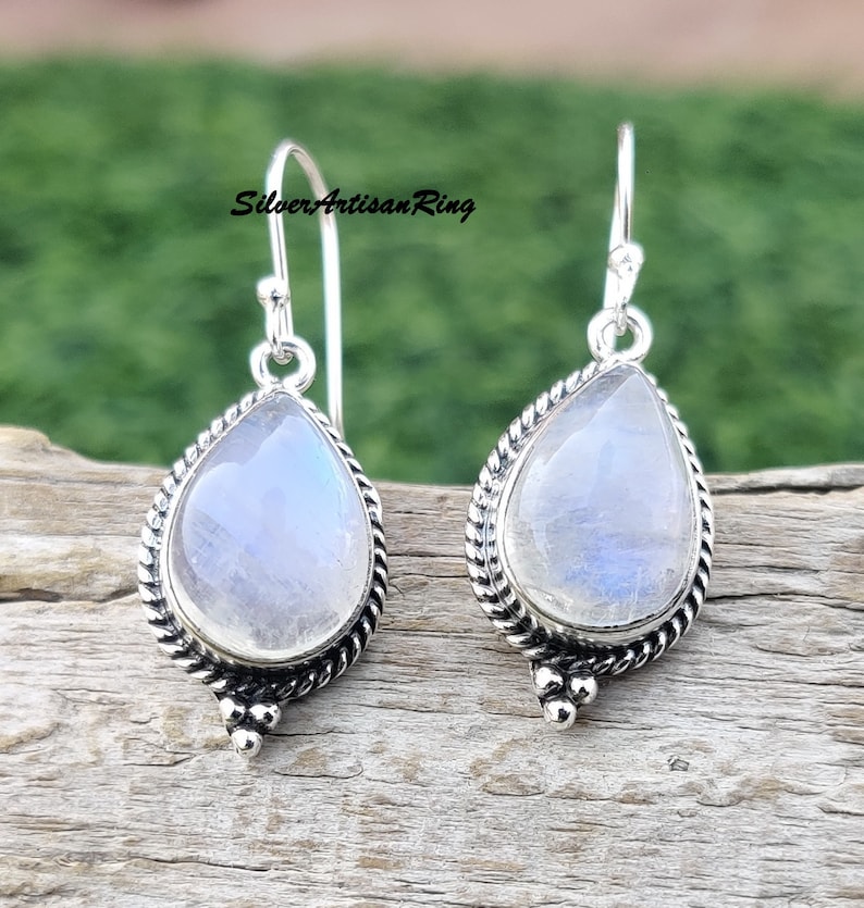 May include: A pair of silver dangle earrings with teardrop-shaped moonstone gemstones. The earrings have a delicate, twisted wire design and are accented with small silver beads.