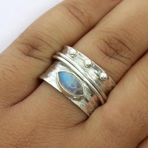 Könnte beinhalten: Silberner Ring mit gehämmertem Muster und einem ovalen, irisierenden Edelstein. Der Ring hat ein drehbares Band und drei kleine, runde Verzierungen auf der Oberseite.