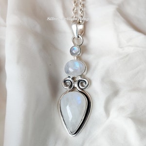 May include: A silver necklace with a teardrop-shaped moonstone pendant. The pendant is surrounded by two smaller moonstones and intricate silver detailing.