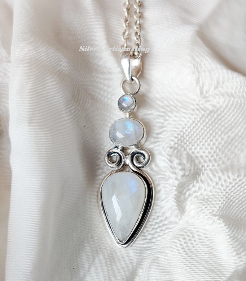 May include: A silver necklace with a teardrop-shaped moonstone pendant. The pendant is surrounded by two smaller moonstones and intricate silver detailing.
