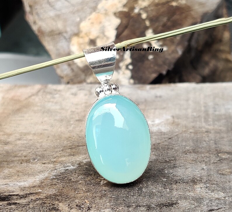 May include: A silver pendant with an oval, light blue gemstone. The gemstone is set in a silver bezel and has a smooth, polished surface. The pendant has a simple, elegant design, suitable for everyday wear.