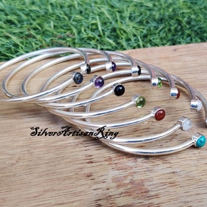 Pode incluir: Um conjunto de oito pulseiras de prata, cada uma com uma gema de cor diferente. As pulseiras t&ecirc;m um design simples e curvo, com uma &uacute;nica gema na extremidade.