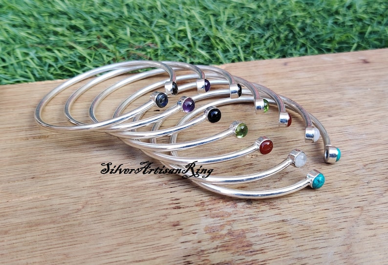 Pode incluir: Um conjunto de oito pulseiras de prata, cada uma com uma gema de cor diferente. As pulseiras t&ecirc;m um design simples e curvo, com uma &uacute;nica gema na extremidade.