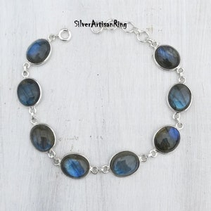 May include: A silver bracelet with a chain link design and oval-shaped labradorite gemstones. The stones have a dark blue and green iridescent sheen.